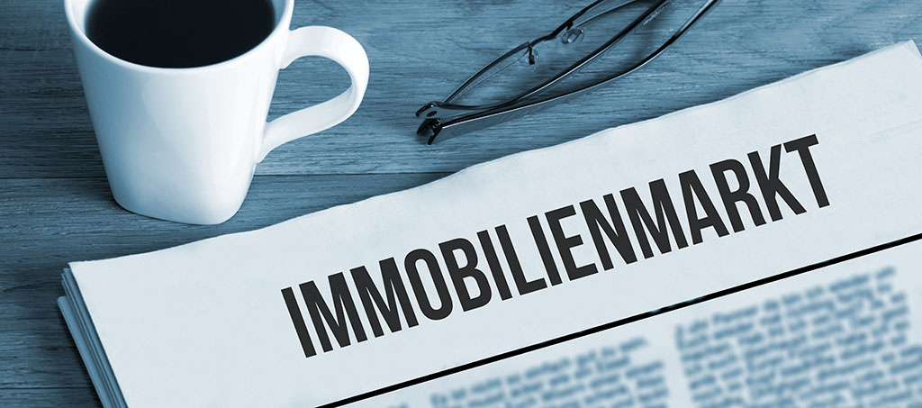 Immobilien-Zeitung, daneben Kaffee, Brille, Stift